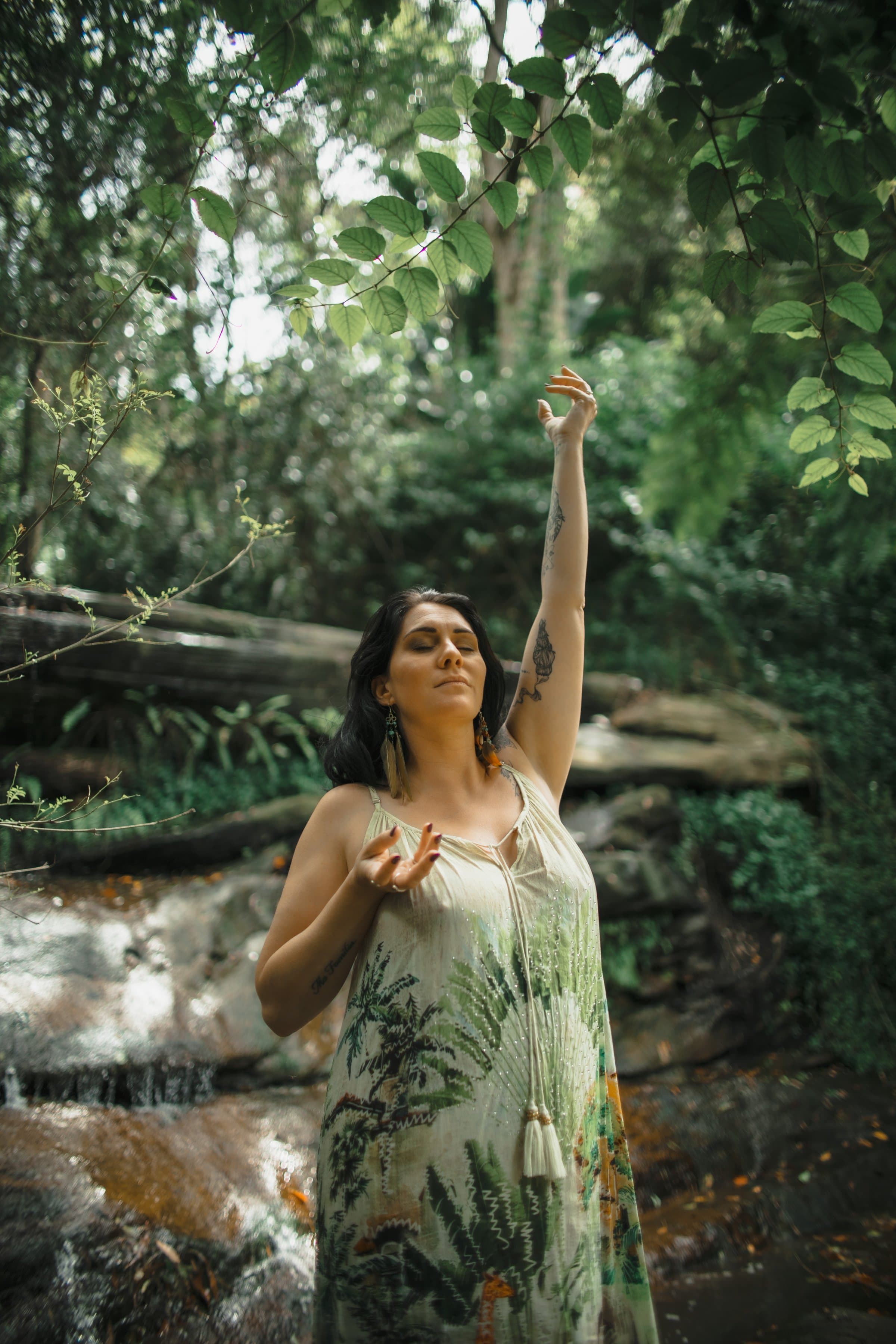 Kati by a waterfall in the rainforest, eyes closed, one arm raised