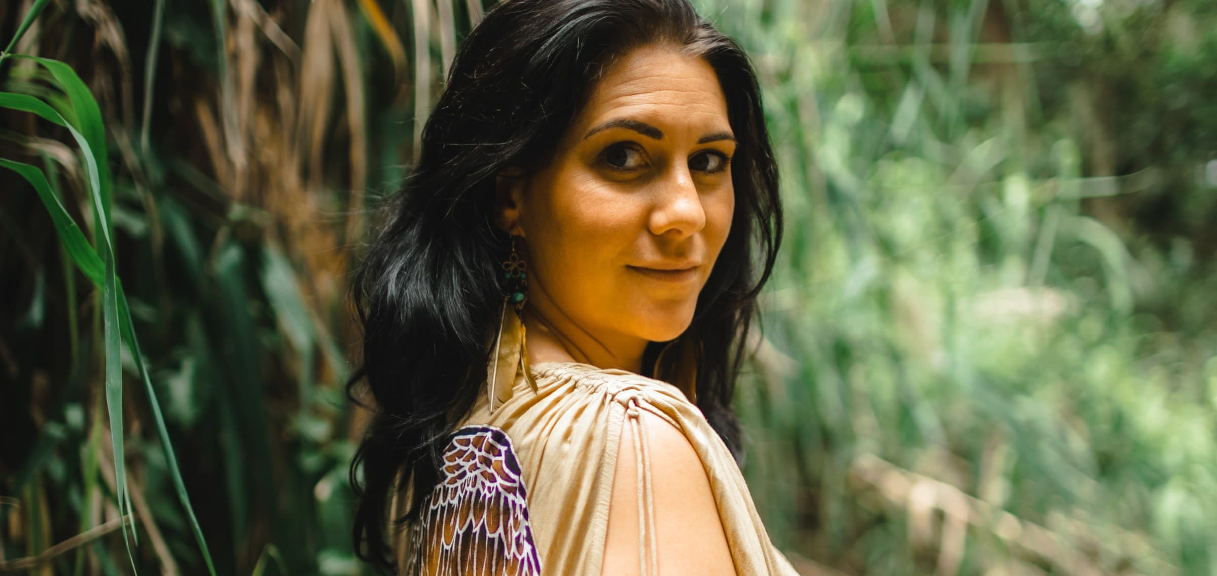 Kati in tall green reeds, looking back over her shoulder in a cream shawl