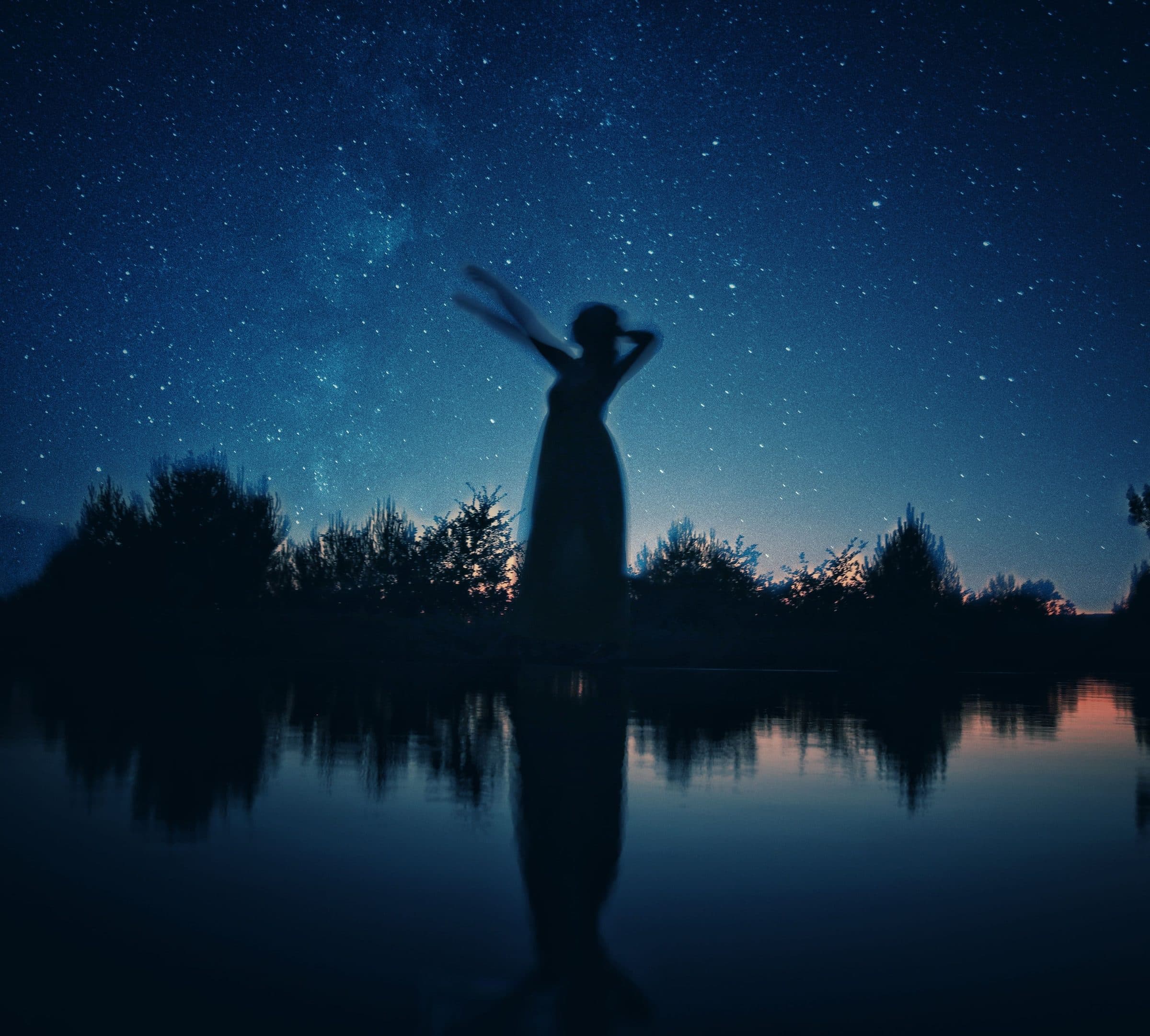 A woman silhouetted under a field of stars, reflected in water