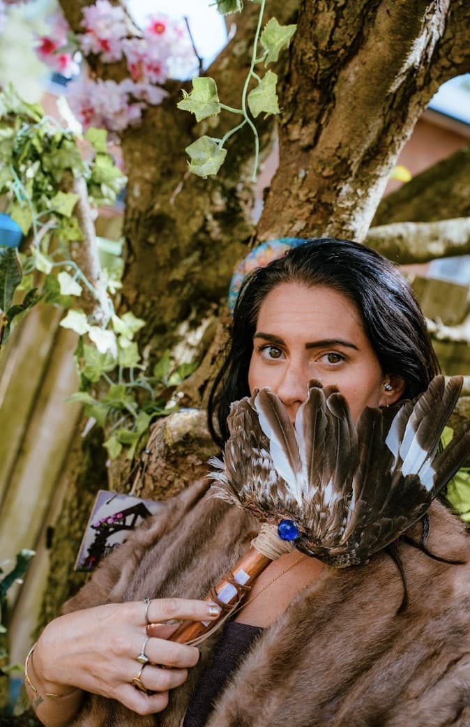 Kati by a tree, a fan of feathers held over her face