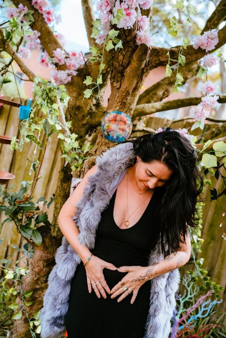 A woman in a garden, hands resting on her womb