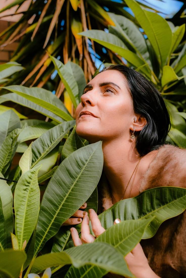 A woman among tropical leaves, her face lifted to the light