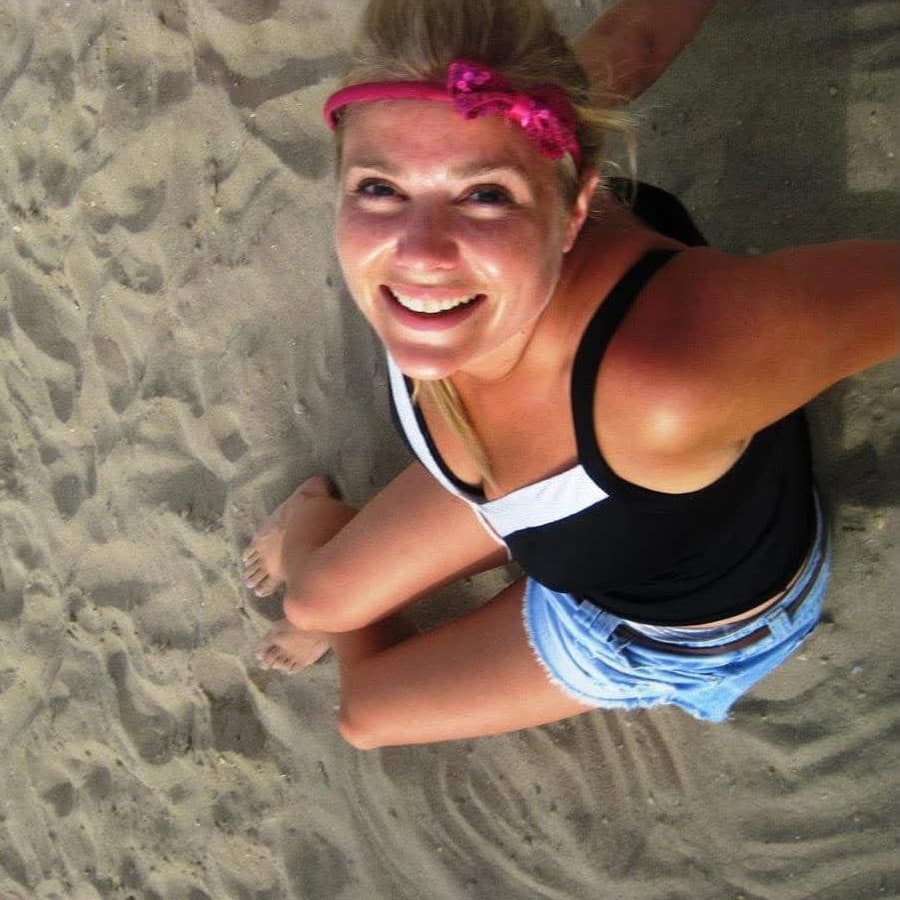 Chelsea Little sitting in the sand, smiling up at the camera